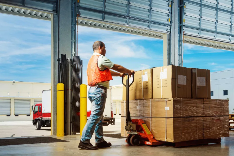A worker moves a pallet of boxes with a pallet truck at a loading dock
