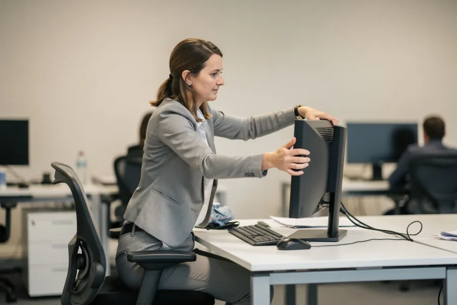 A woman adjusts a computer monitor at her desk