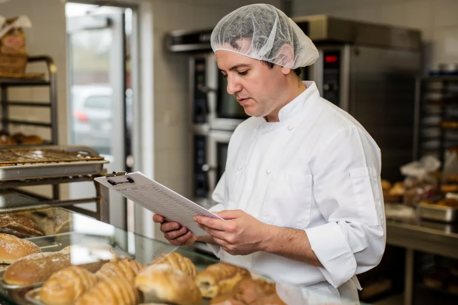 A chef checks a clipboard beside a tray of pastries